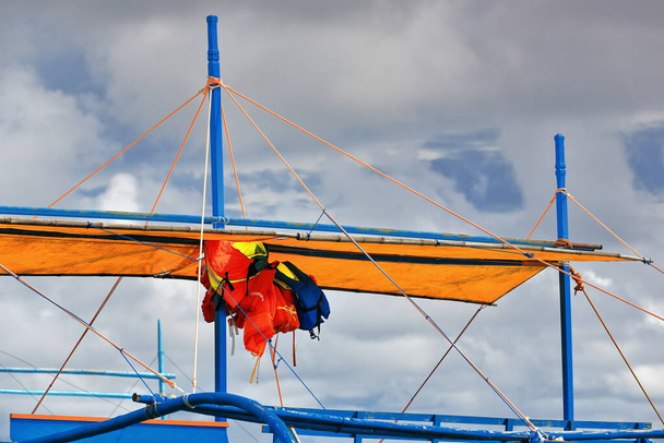 Life vests hanging under canvas awning-balangay or bangka double outrigger boat for use of the nearby tourist resorts stranded on Punta Ballo beach. Sipalay-Negros Occidental-West Visayas-Philippines. - Foto, Imagen