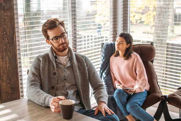 Couple in kitchen spending time together with cup of coffee and smartphone - Photo, Image