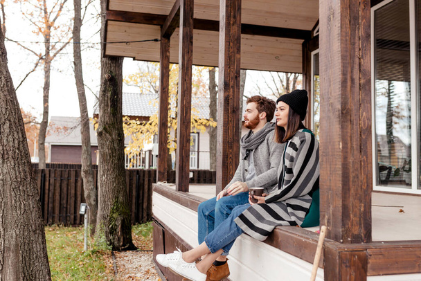 feliz jovem casal sentado ao ar livre, na frente de sua nova casa no dia de outono
 - Foto, Imagem
