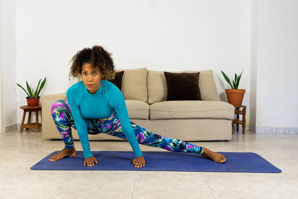 Brasiliano nero giovane donna formazione yoga a casa con il computer portatile in soggiorno. Esercizio su un tappeto. - Foto, immagini