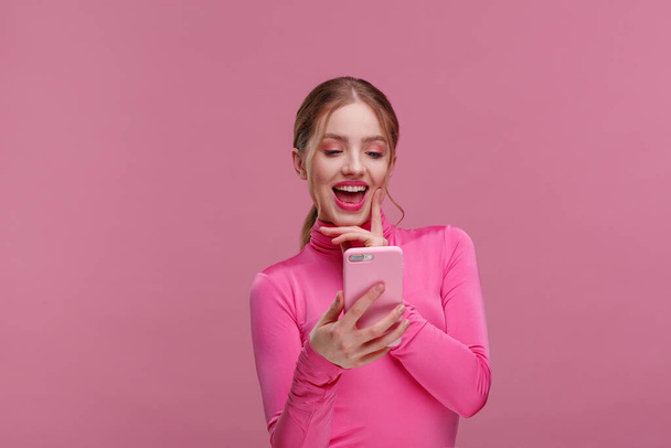 Le meilleur jour de ma vie. Jeune femme rousse surprise tenant un smartphone rose, souriant et exprimant sa positivité. La fille heureuse a eu des nouvelles positives choquantes. Espace de copie. Jeunes travaillant avec des appareils mobiles - Photo, image