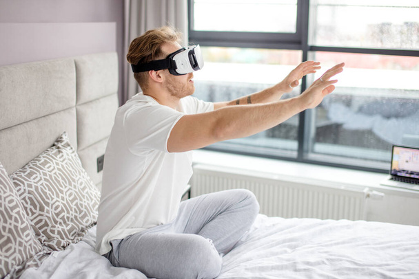 guy is sitting on the bed and trying to touch virtual reality - Foto, Imagem