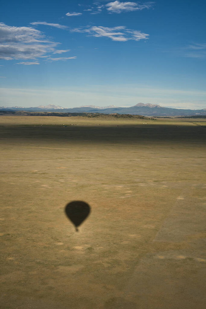 Schatten des Heißluftballons blickt über riesiges Flugzeug mit in der Ferne sichtbaren felsigen Bergen - Foto, Bild