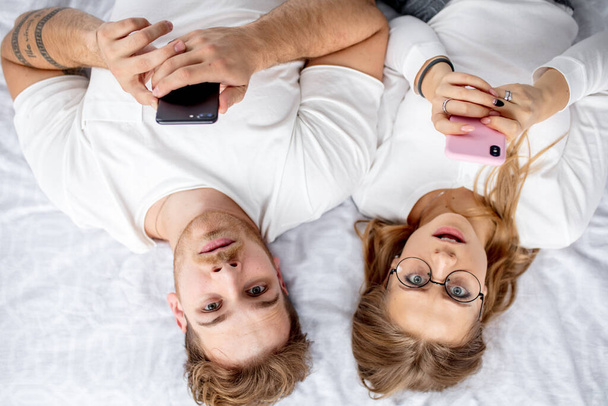 two young emotional surprised people are holding smartphones and looking at the camera - Foto, Bild