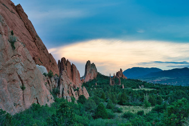 Jumalten puutarha värikkäällä auringonlaskulla. Kauniit värit valavat Colorado-jousien kallioperään. Värikkäitä pilviä, vihreitä puita, ja oranssi kiviä näkyvissä - Valokuva, kuva