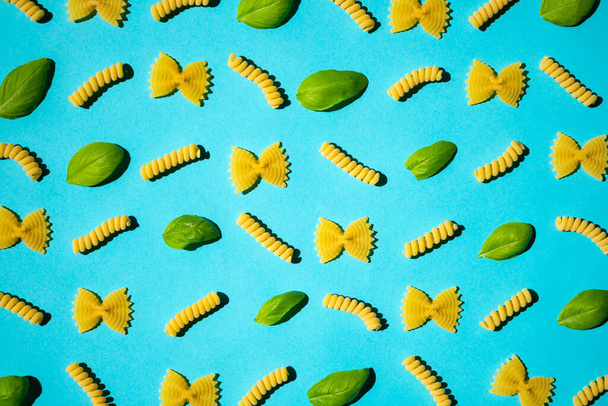 Uncooked curly pasta and basil leaf pattern on blue background. Traditional dry raw macaroni pattern. Nobody - Photo, image