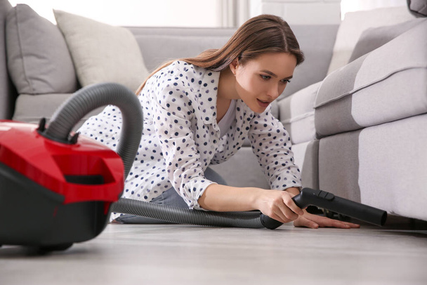Young woman using vacuum cleaner at home - Fotó, kép