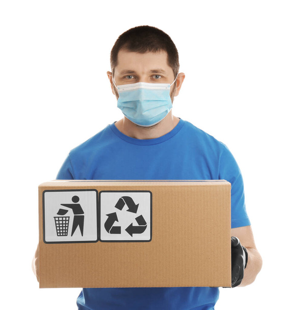 Courier in mask holding cardboard box with different packaging symbols on white background. Parcel delivery - 写真・画像