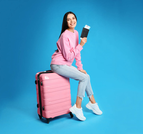 Beautiful woman with suitcase and ticket in passport for summer trip on blue background. Vacation travel - Foto, afbeelding