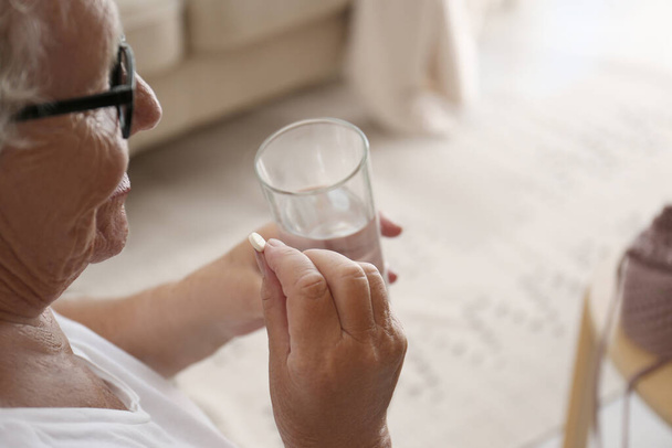 Senior woman with glass of water taking pill at home, closeup - Fotografie, Obrázek