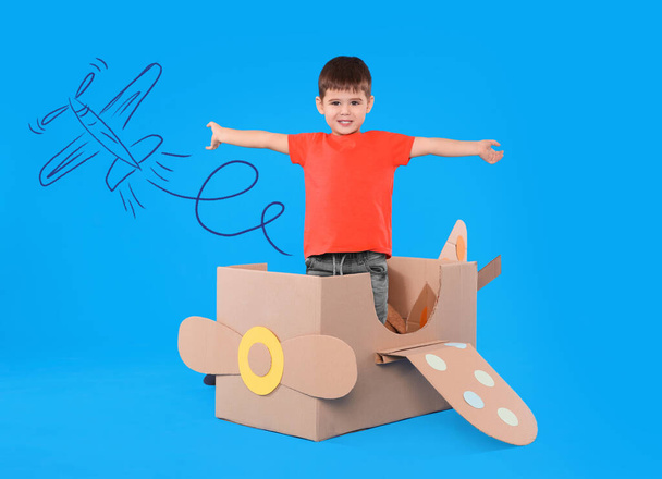 Cute little child playing in cardboard airplane on blue background with illustration - Foto, Bild