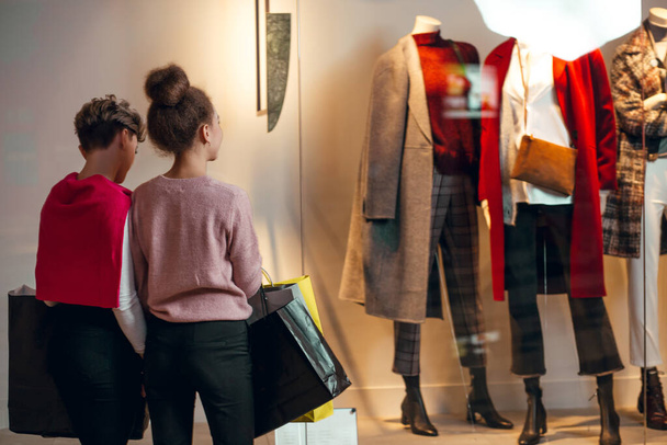 Two women standing in front of women collection boutique, rear view. - 写真・画像