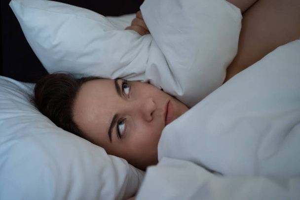 Mujer joven insomnio cubierto la cabeza con almohada, no puede dormir por el ruido de los vecinos, persona frustrada perturbada infeliz en la noche - Foto, imagen