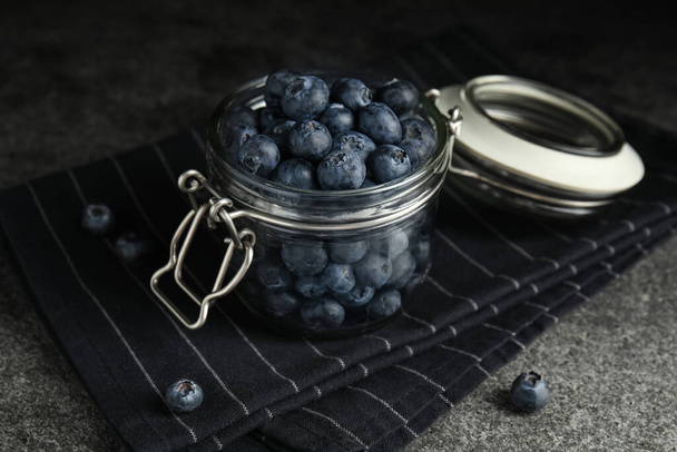 Tasty ripe blueberries in glass jar on grey table - Foto, imagen