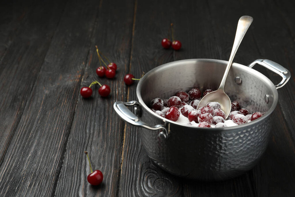 Pot with cherries and sugar on black wooden table, space for text. Making of delicious jam - Foto, imagen