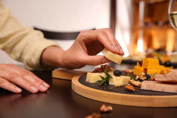 Woman taking piece of delicious cheese at table indoors, closeup - Fotó, kép
