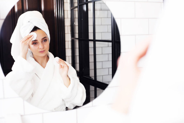 Sorrindo jovem mulher lavar o rosto com esponja de limpeza facial no banheiro
 - Foto, Imagem