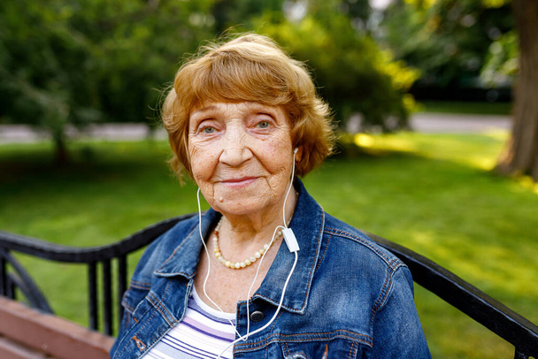 緑の草と笑顔に対するカメラを見てヘッドフォンを持つ高齢女性の肖像画。クローズアップポートレート、ソフトフォーカス - 写真・画像