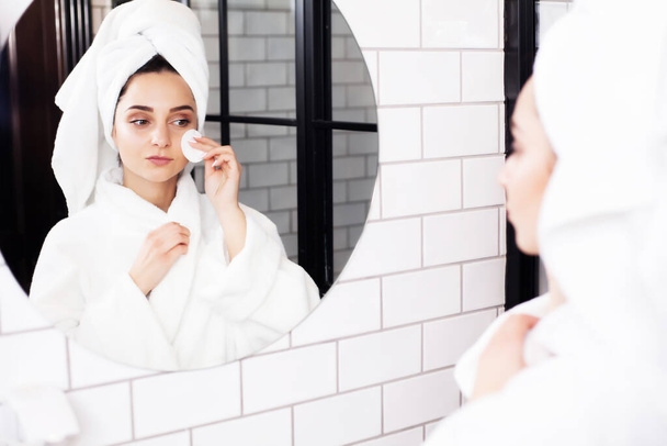 Souriante jeune femme se lave le visage avec une éponge de nettoyage du visage à la salle de bain - Photo, image