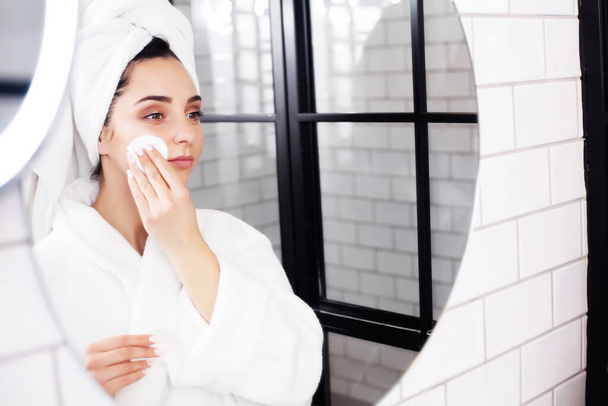 Mujer joven sonriente lavándose la cara con esponja de limpieza facial en el baño - Foto, imagen