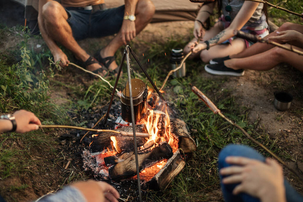 peoples arms holding branches with sausages above the campfire - Photo, Image