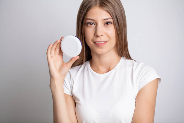 Jeune jolie femme tenant crème cosmétique hydratante - Photo, image