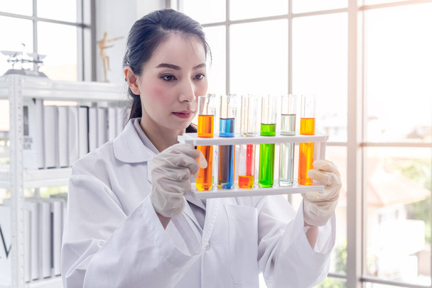 Ασιάτισσες επιστήμονας κατέχουν και αναζητούν δοκιμαστικό σωλήνα που διεξάγει έρευνα ανάμειξη χημεία στο εργαστήριο. - Φωτογραφία, εικόνα