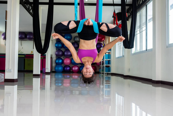 Young pretty slim body fitness girl practicing fly yoga in the gym - Photo, Image