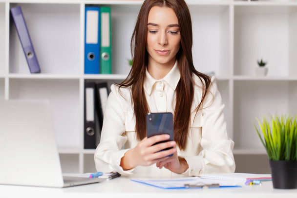 Aantrekkelijke vrouw werkt aan smartphone in haar werkstation. - Foto, afbeelding
