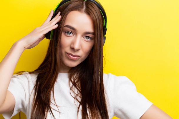 Kaunis nuori seksikäs tyttö DJ kuuntelee musiikkia vihreillä kuulokkeilla keltaisella taustalla - Valokuva, kuva