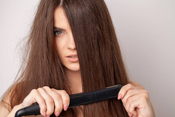 Γυναίκα με όμορφα μακριά ίσια μαλλιά χρησιμοποιώντας ένα ισιωτικό μαλλιών - Φωτογραφία, εικόνα