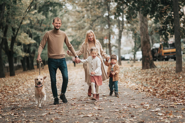 happy Caucasian family walking in autumn park, Mother father son daughter and dog Labrador, fall season - Photo, Image