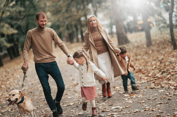 happy Caucasian family walking in autumn park, Mother father son daughter and dog Labrador, fall season - Foto, Imagen