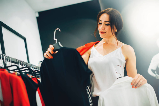 Which one? Beautiful young woman stylist designer trying to choose clothes to herself or customer while working in fashion boutique. Fashion stylist show new collection and trends in store - Fotó, kép