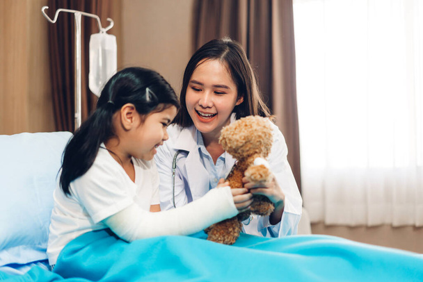 Asiático sorrindo mulher médico serviço ajudar apoio discutir e consultoria falar com menina paciente dar ursinho de pelúcia e verificar as informações no hospital - Foto, Imagem