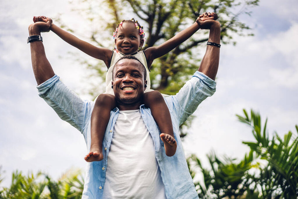 Πορτρέτο του απολαύσετε ευτυχισμένη αγάπη μαύρο οικογένεια αφροαμερικανός πατέρας μεταφέρουν κόρη μικρό κορίτσι της Αφρικής χαμογελώντας και διασκεδάζοντας στιγμές διασκέδασης καλή στιγμή στο πάρκο καλοκαίρι στο σπίτι - Φωτογραφία, εικόνα