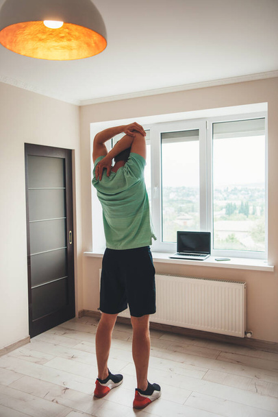 arrière vue photo d'un homme caucasien faisant remise en forme à la maison à l'aide d'un ordinateur portable près de la fenêtre - Photo, image