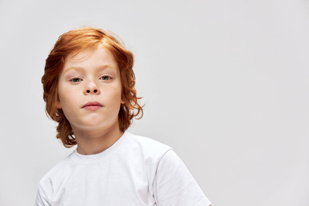 cute red-haired boy with freckles on face wearing white t-shirt gray isolated background  - Foto, Imagem