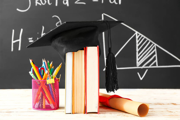 Выпускная шляпа, книги, канцелярские принадлежности и диплом на столе в классе - Фото, изображение