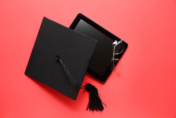 Graduation hat, tablet computer and glasses on color background - Photo, Image