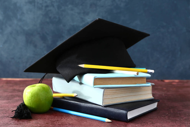 Sombrero de graduación, libros y manzana en la mesa - Foto, imagen