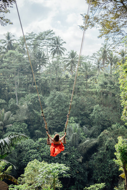 Nainen punaisessa mekossa nauttia loma toimintaa istuu jättiläinen keinu Balilla, Indonesiassa. - Valokuva, kuva