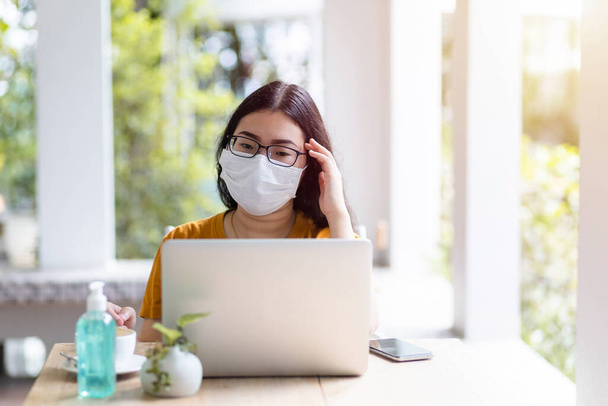 Stressed of freelance people business female wearing protective mask casual having a headache after business losses working with laptop in coffee shop background,working from home,Concept of COVID-19 - Photo, Image