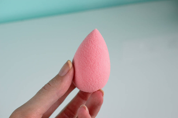 Pink beauty tear-shaped blender, clean egg-shaped sponge isolated on light background. Cosmetic tool for makeup in hand. - Photo, Image