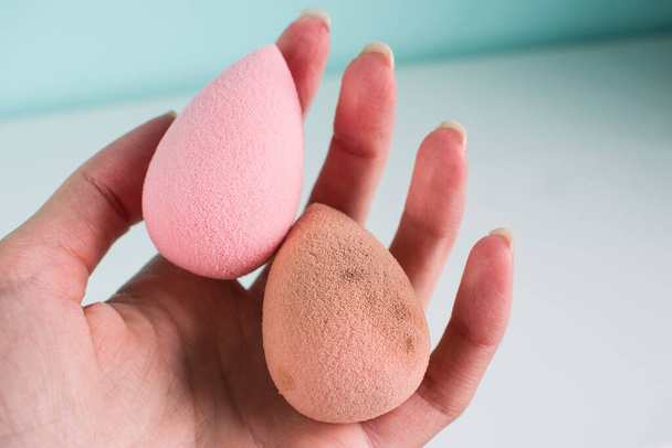 Batidora rosa con forma de lágrima, esponjas sucias y limpias en forma de huevo aisladas sobre fondo claro. Herramienta cosmética para maquillaje en mano. - Foto, Imagen