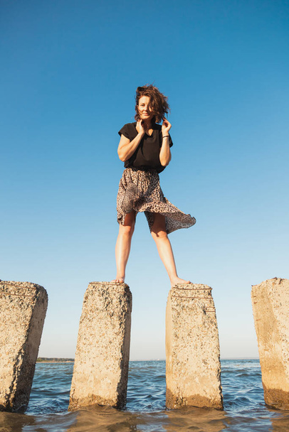 Une promenade romantique d'une femme aux cheveux bouclés dans une robe posant sur la pierre dans la mer. Le concept de liberté, d'émancipation et d'amour des femmes - Photo, image