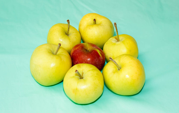 Ένα ώριμο Κόκκινο Μήλο ανάμεσα σε πράσινα μήλα σε ένα ελαφρύ φόντο. Η έννοια της επιλογής και επιλογής από ένα κοινό σωρό. Επιλεκτική βολή. - Φωτογραφία, εικόνα