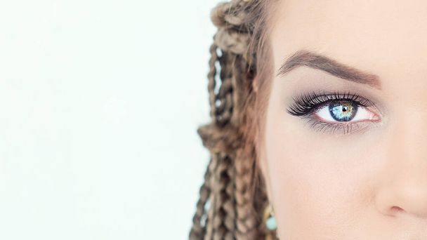 Artista de maquiagem profissional trabalhando com bela jovem. modelo loira brilhante com tranças africanas em um fundo branco
 - Foto, Imagem