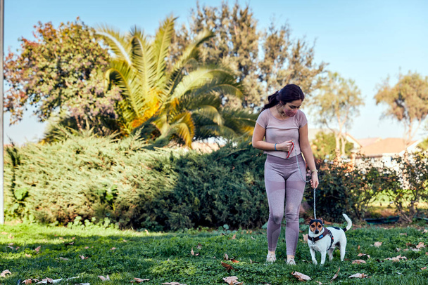 公園でマスクをした若い女性が伝染病の流行の最中に犬を安全に歩く犬の恋人の概念 - 写真・画像
