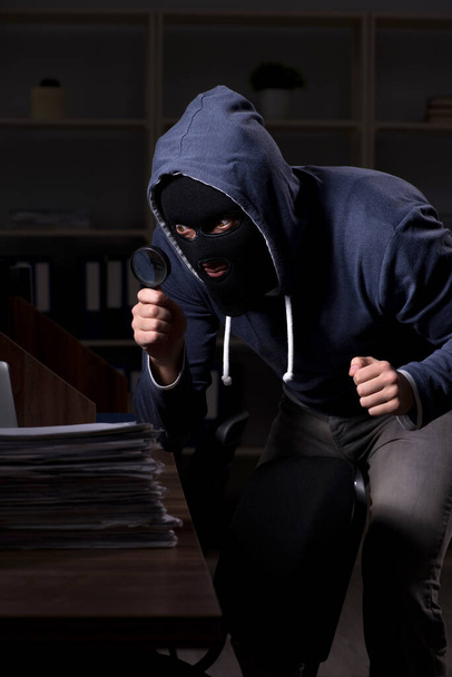 Hombre ladrón en pasamontañas en la oficina la noche
 - Foto, imagen